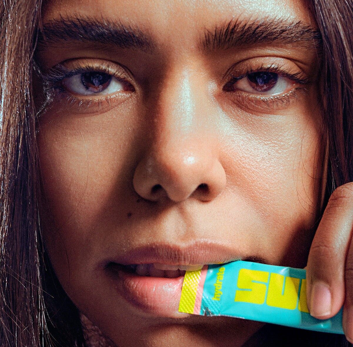 A woman holding a turquoise SULT electrolyte sachet to her lips