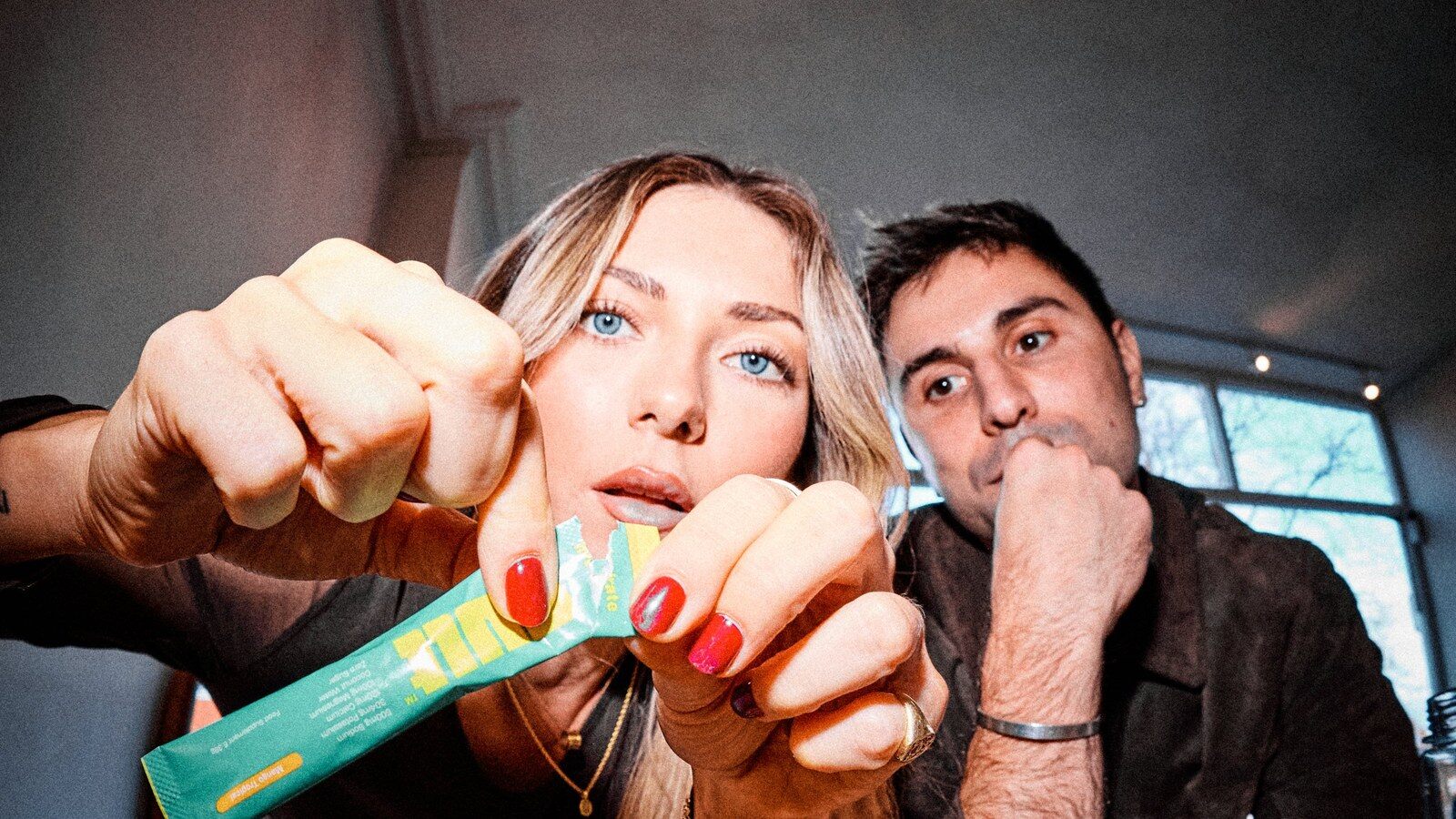 A woman tearing open a turquoise SULT electrolyte sachet at a table while a man watches