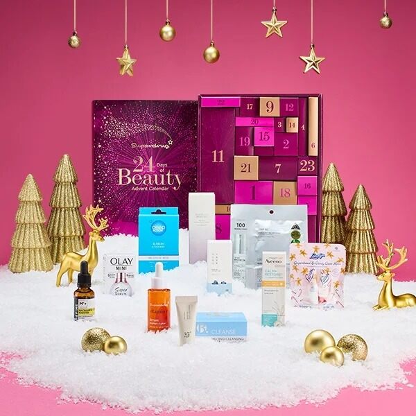 The Superdrug 24 Days of Beauty advent calendar 2026 with its skincare products on artificial snow, gold trees and a pink background