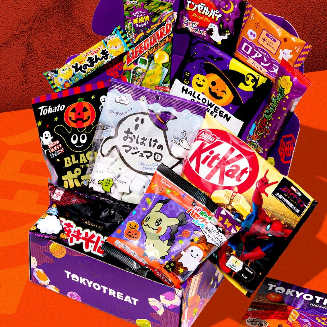 A purple and orange TokyoTreat Halloween box overflowing with Japanese snacks, including a KitKat and Pokémon packets