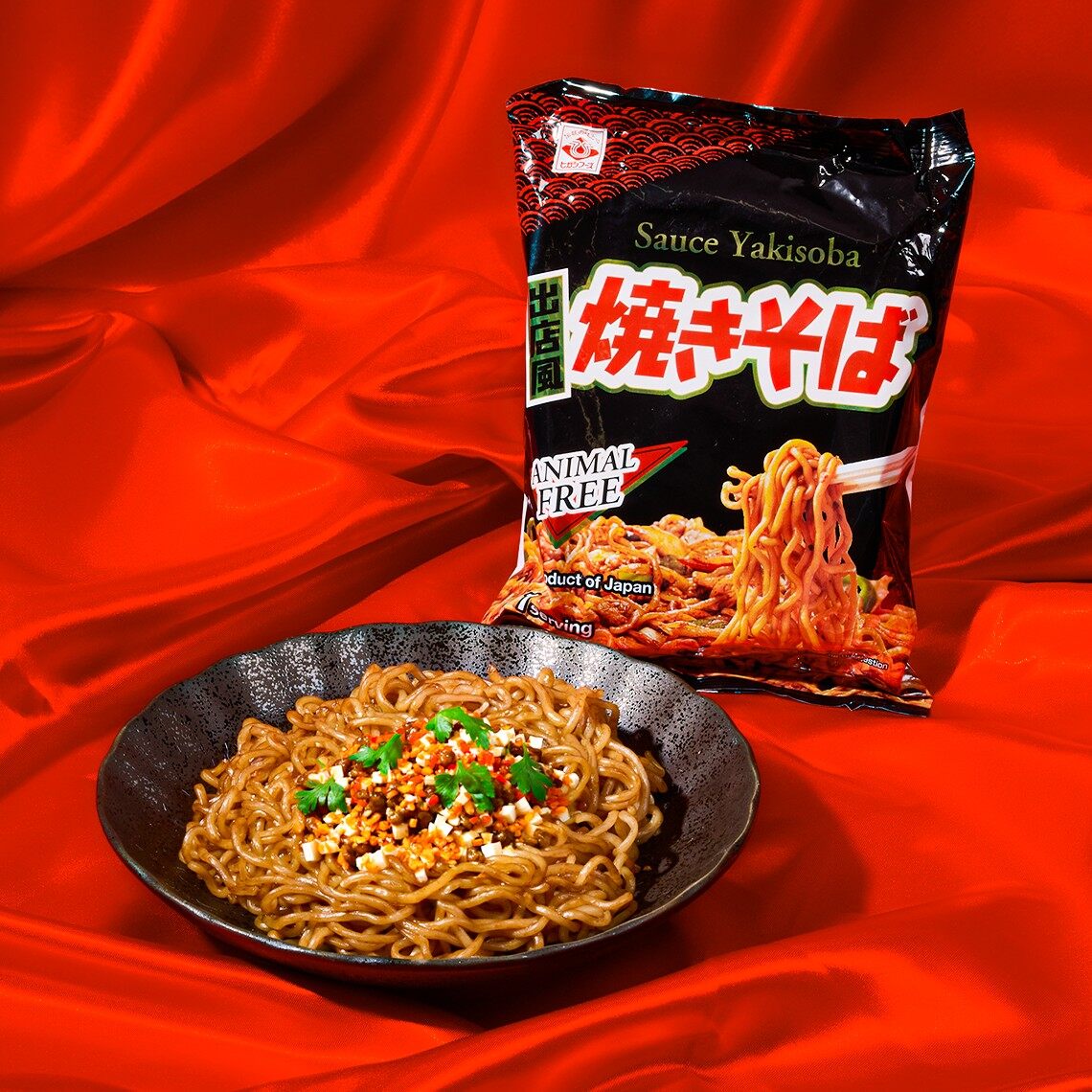 A pack of Japanese yakisoba noodles next to a bowl of cooked noodles on a red background