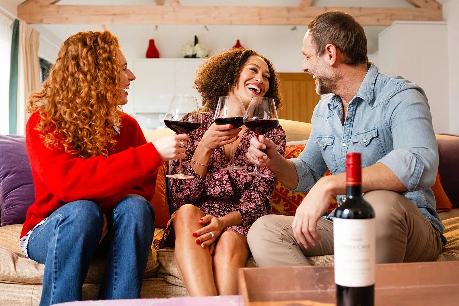 Three friends sharing red wine on a sofa