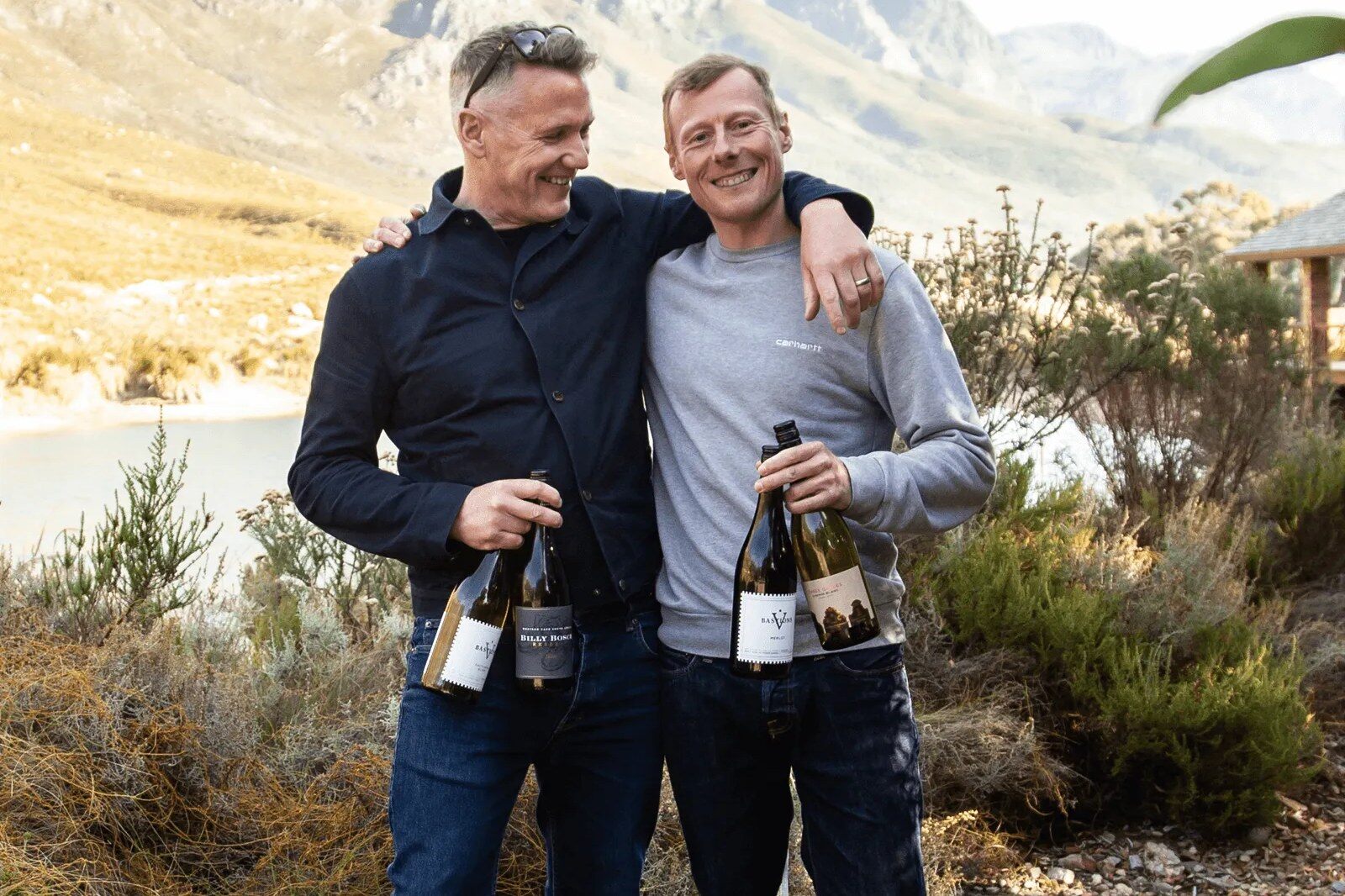 Two winemakers holding bottles of wine in front of mountains