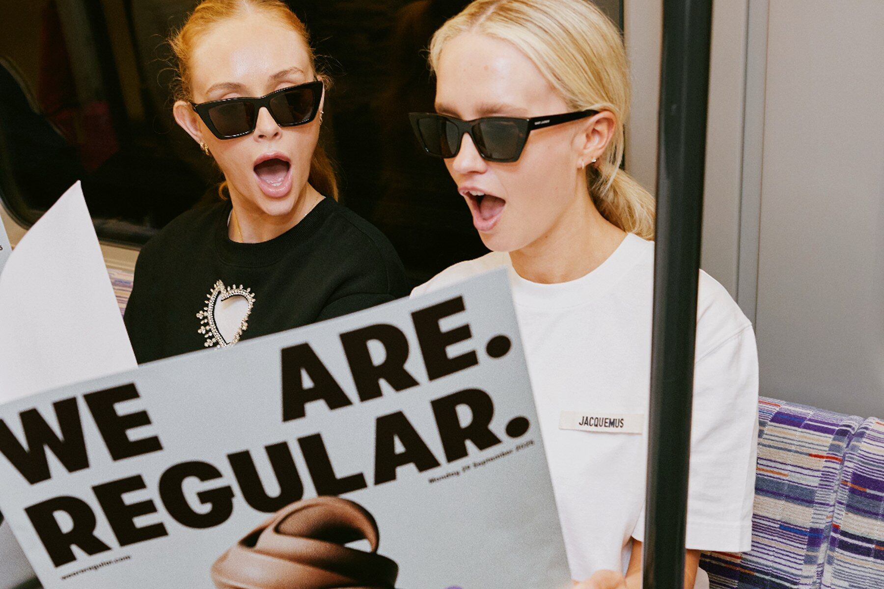 Two women on the London Underground holding We Are Regular posters