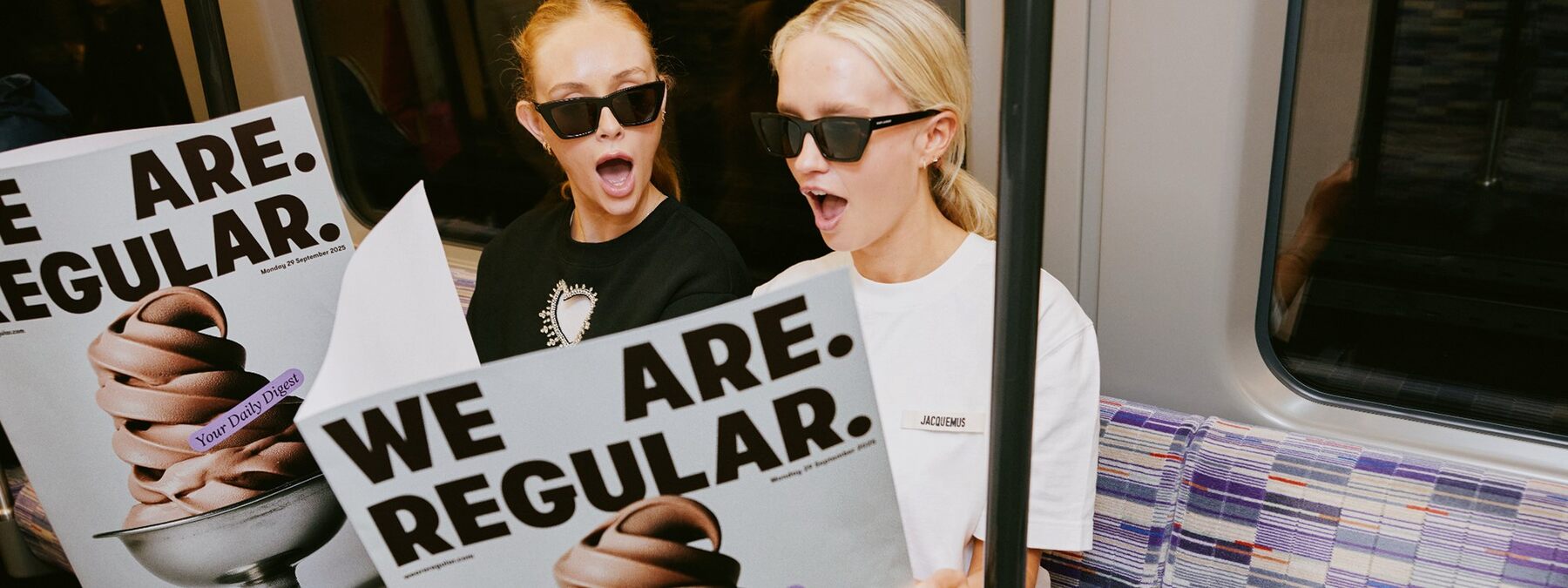 Newspaper-style We Are Regular posters held by two readers in sunglasses on a Tube carriage