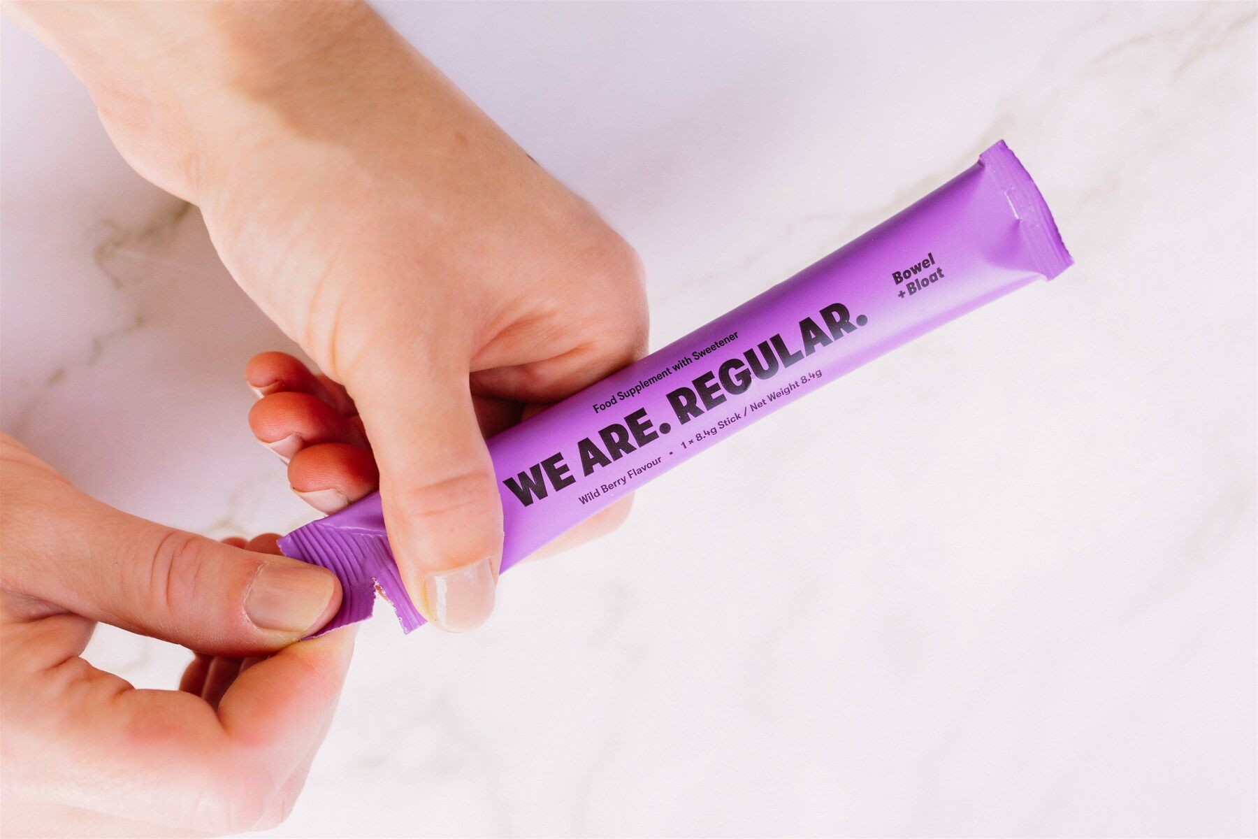 A hand tearing open a We Are Regular powder stick