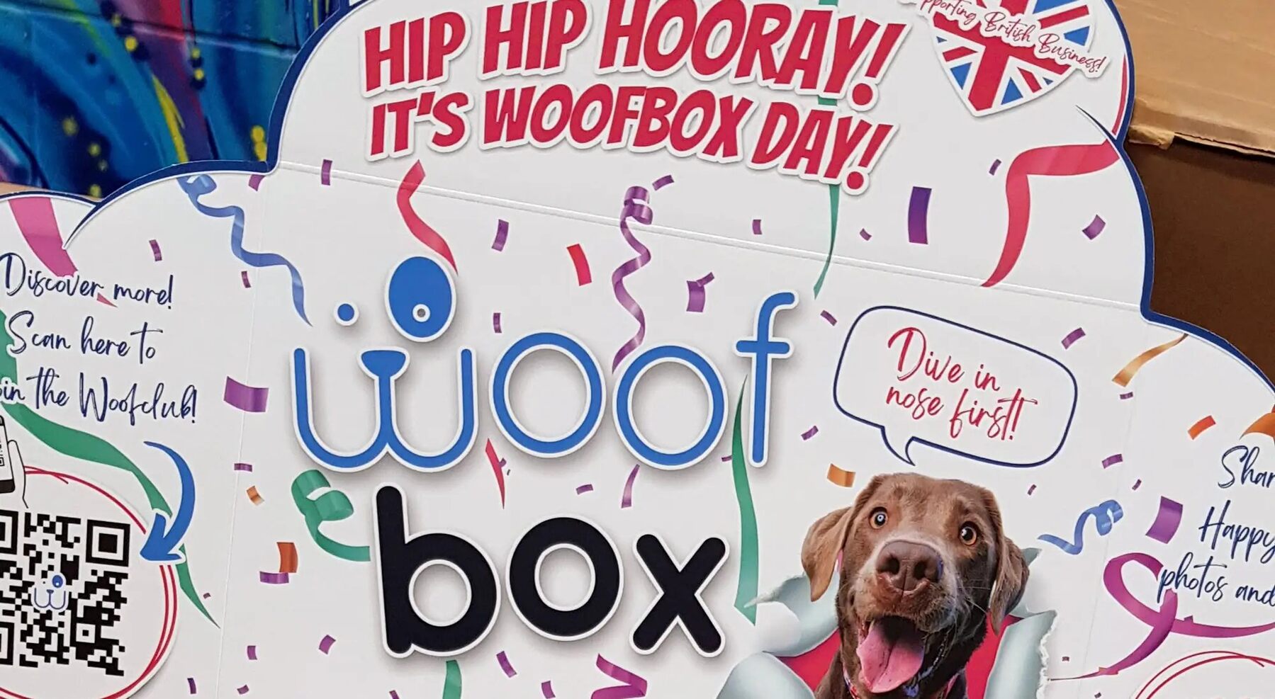 The inside of a Woofbox lid reading Hip Hip Hooray, it's Woofbox Day, with a chocolate Labrador and confetti