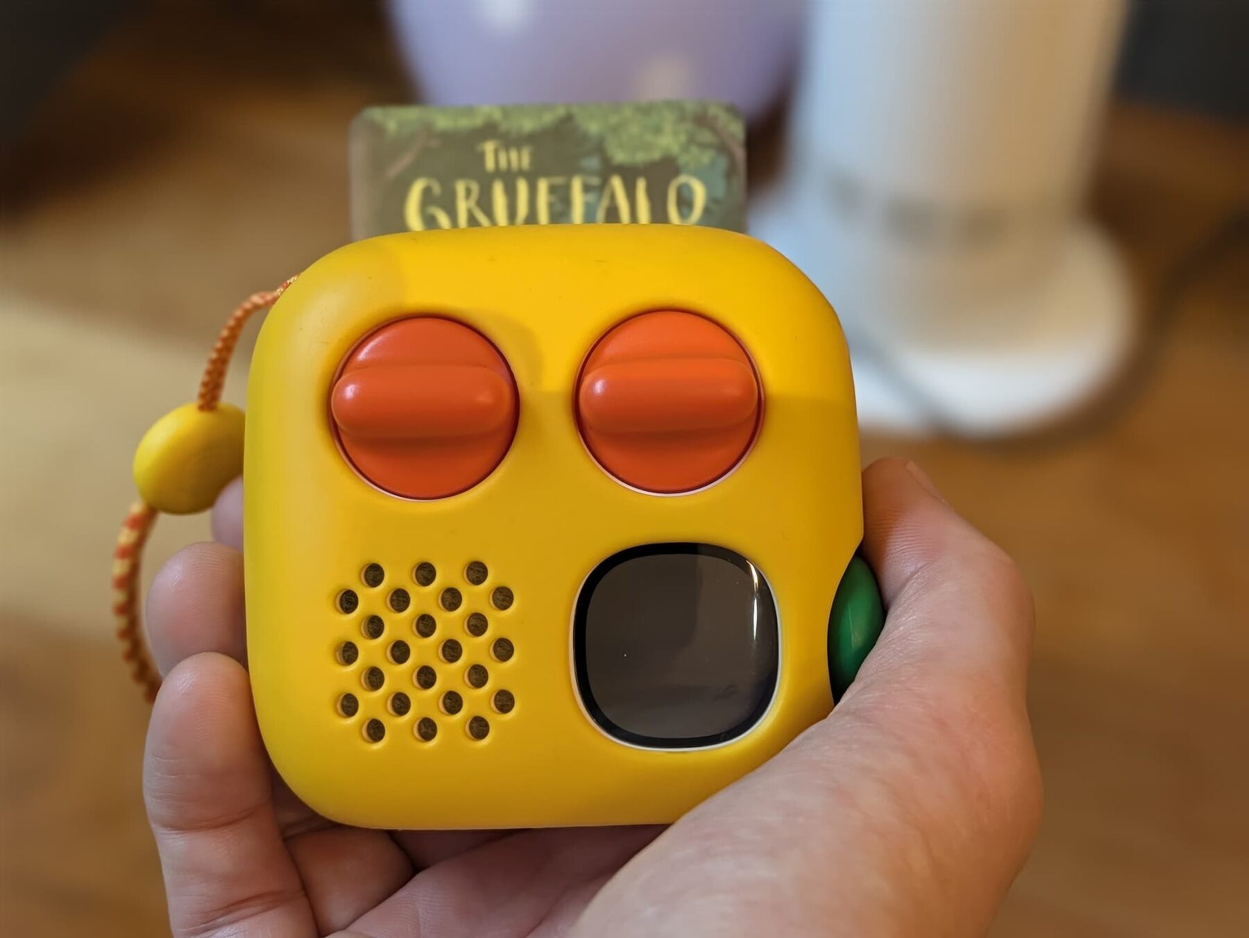 A yellow Yoto Mini 4th Gen held in an adult's hand, with The Gruffalo card in the slot, two orange knobs and the green button